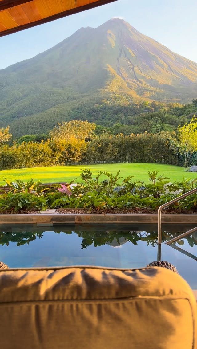 Luxury lodge pool overlooking lush greenery and a large conical volcano mountain.