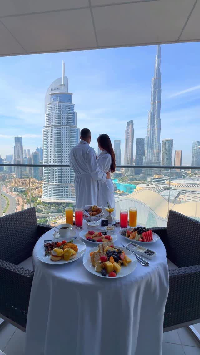 Couple in bathrobes overlooking Dubai skyline with a breakfast spread on a balcony