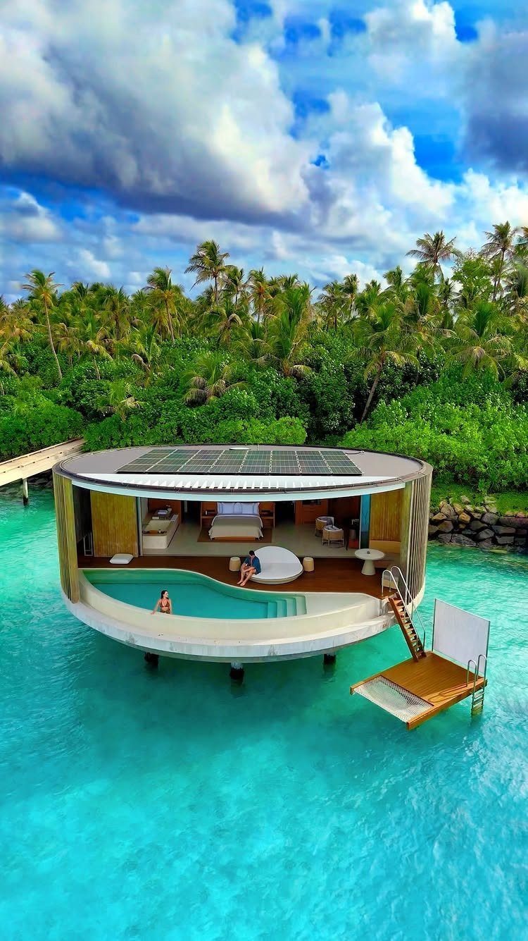 Circular overwater bungalow with private pool in turquoise water surrounded by tropical palms.