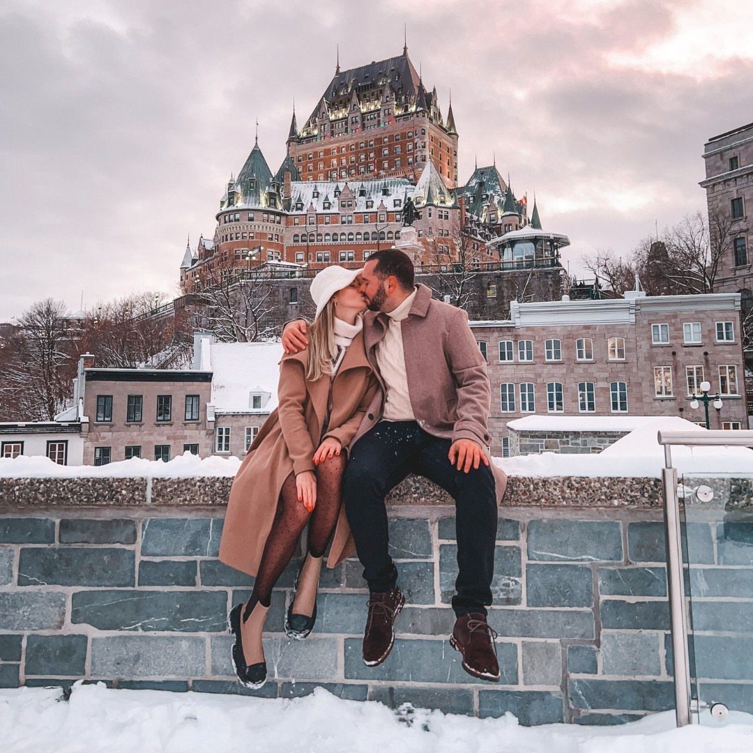 Couple kissing on a stone wall with the Château Frontenac in snowy Quebec City.