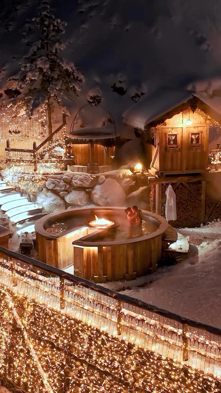 Couple in a wooden hot tub surrounded by snow and warm fairy lights