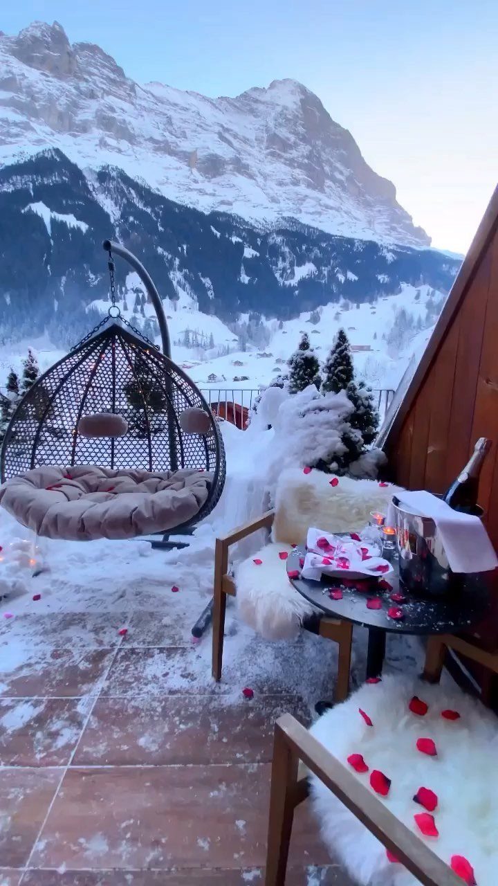 Romantic snowy balcony with champagne and rose petals overlooking majestic winter mountains.