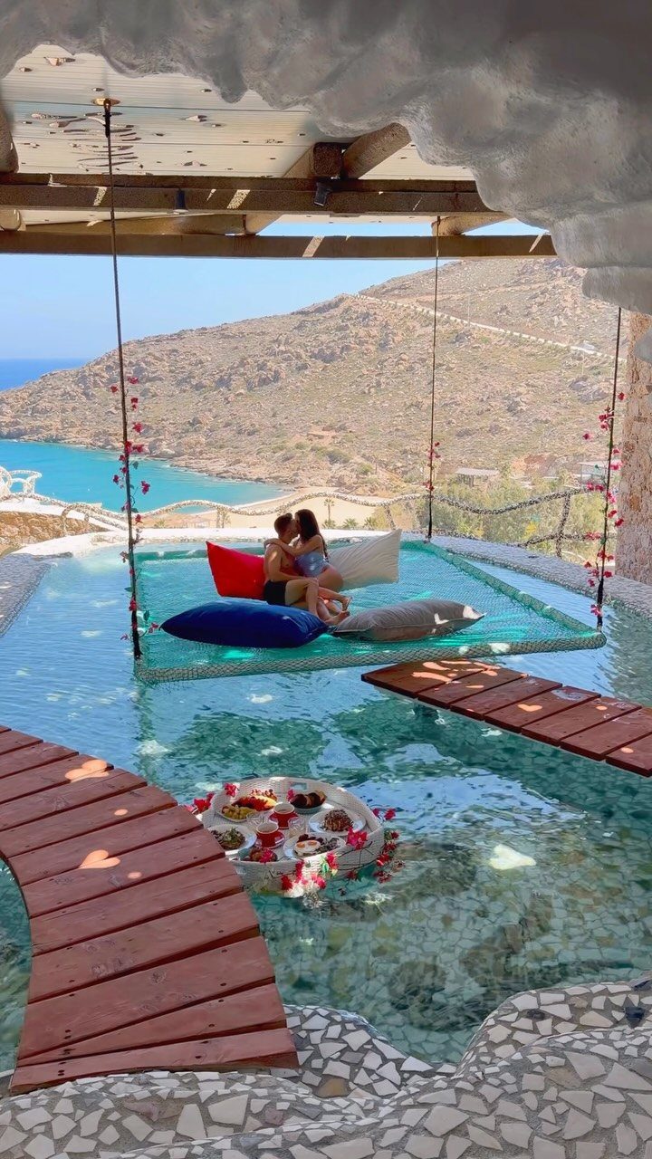 Couple relaxing on a floating bed in a luxury pool overlooking Greek coastline