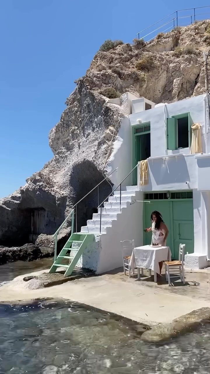 Woman dining at a white table beside a cliffside house in Milos, Greece.