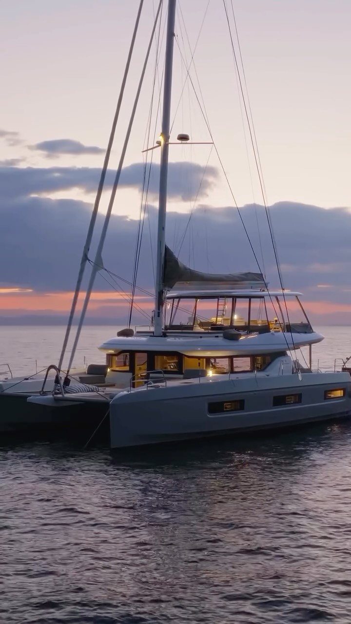 White luxury catamaran sailboat floating on calm water during a purple sunset.