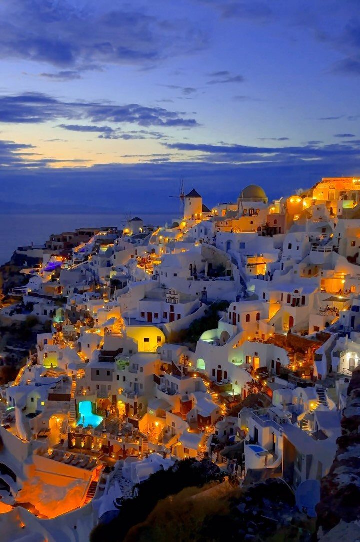 White-washed buildings of Santorini village illuminated at dusk with a traditional windmill.
