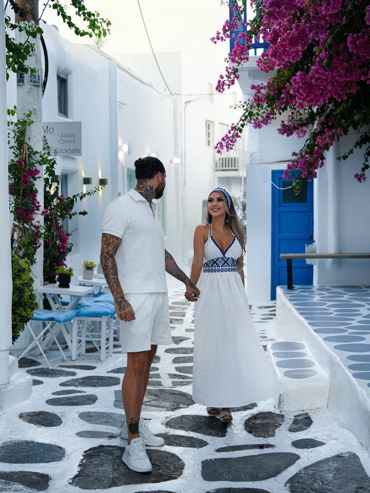 Couple walking through a white village street with blue doors and pink flowers.