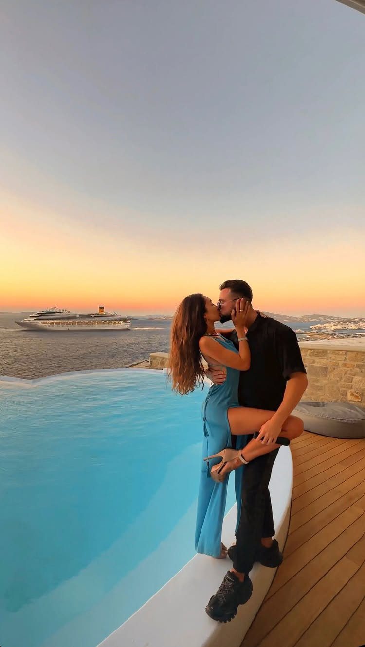 Couple kissing by an infinity pool overlooking the ocean with a cruise ship at sunset