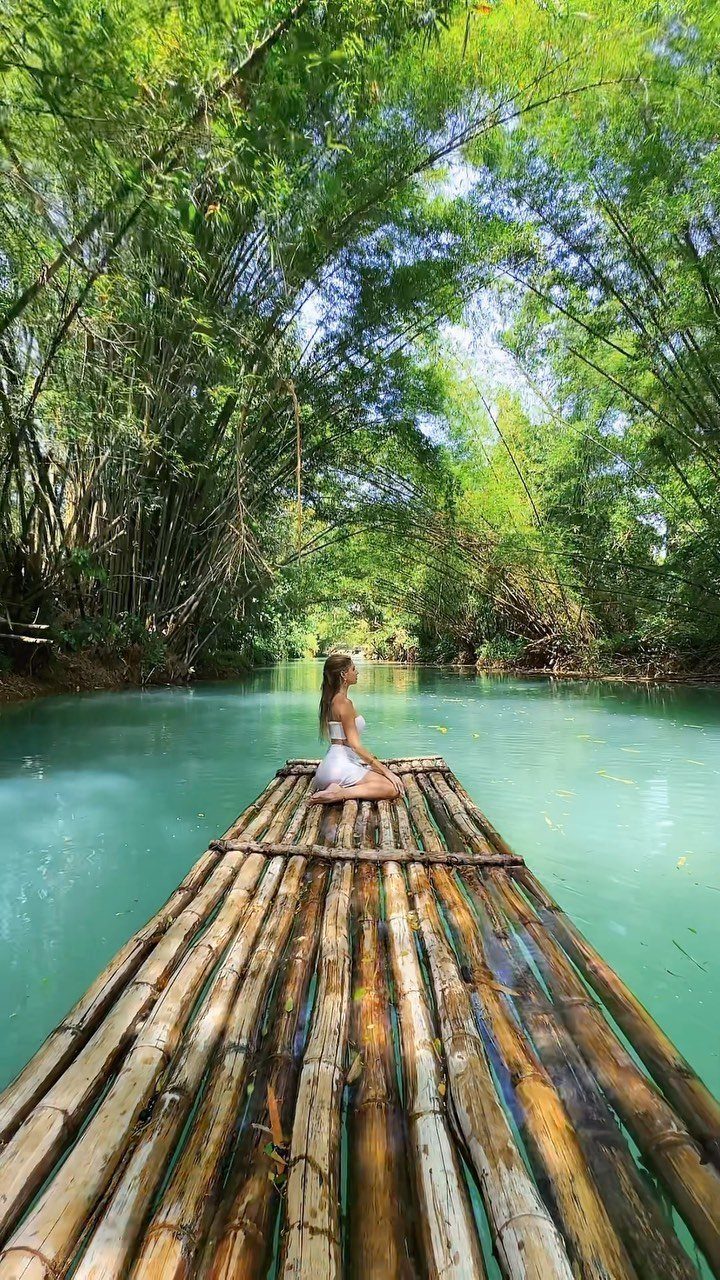 Woman in white dress sitting on a bamboo raft on a turquoise river.