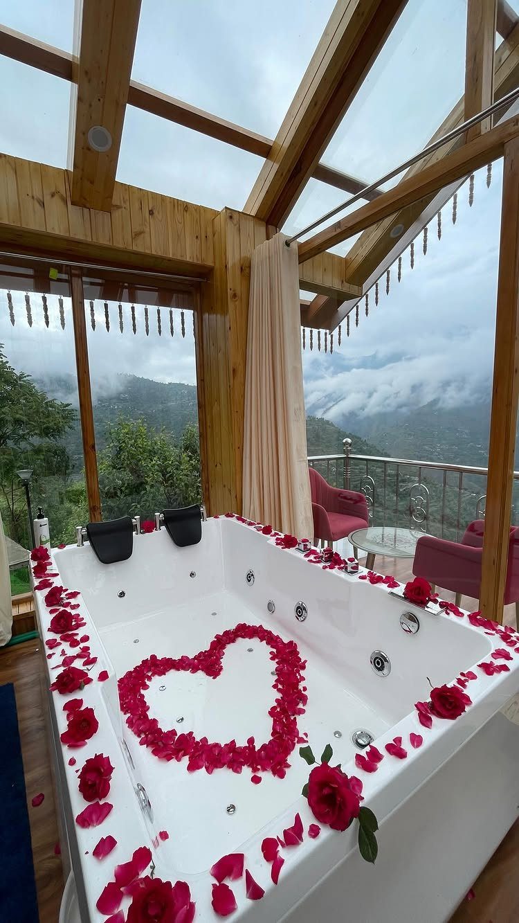 White jacuzzi tub with red rose petals in a heart shape overlooking misty mountains.