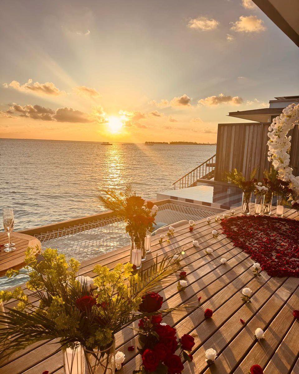 Wooden deck decorated with rose petals and flowers overlooking a golden ocean sunset.