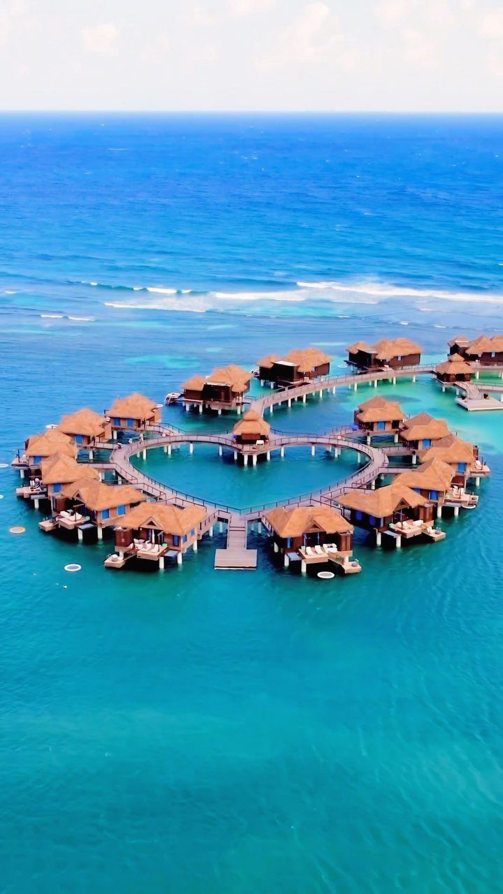 Heart-shaped arrangement of luxury overwater bungalows with thatched roofs in turquoise ocean water.