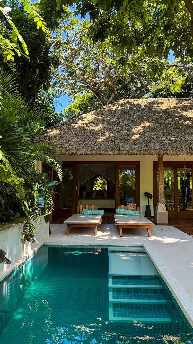 Luxury tropical villa with a thatched roof, turquoise pool, and wooden lounge chairs.