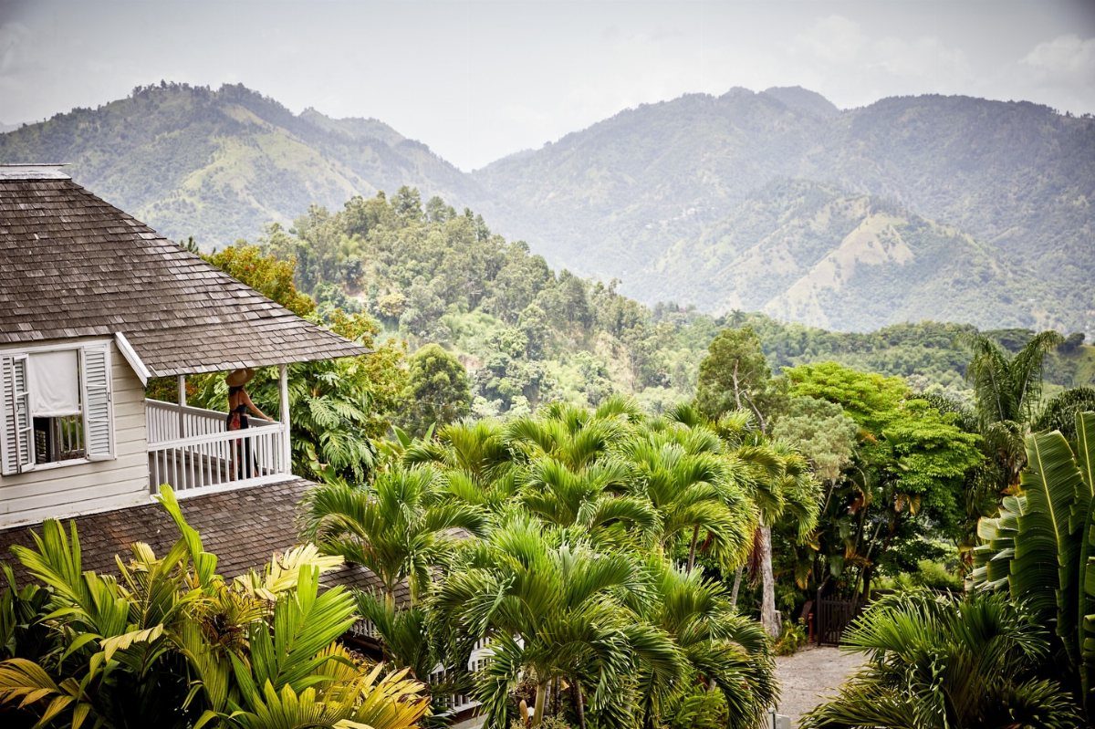 White boutique hotel balcony overlooking lush tropical greenery and distant blue mountains.