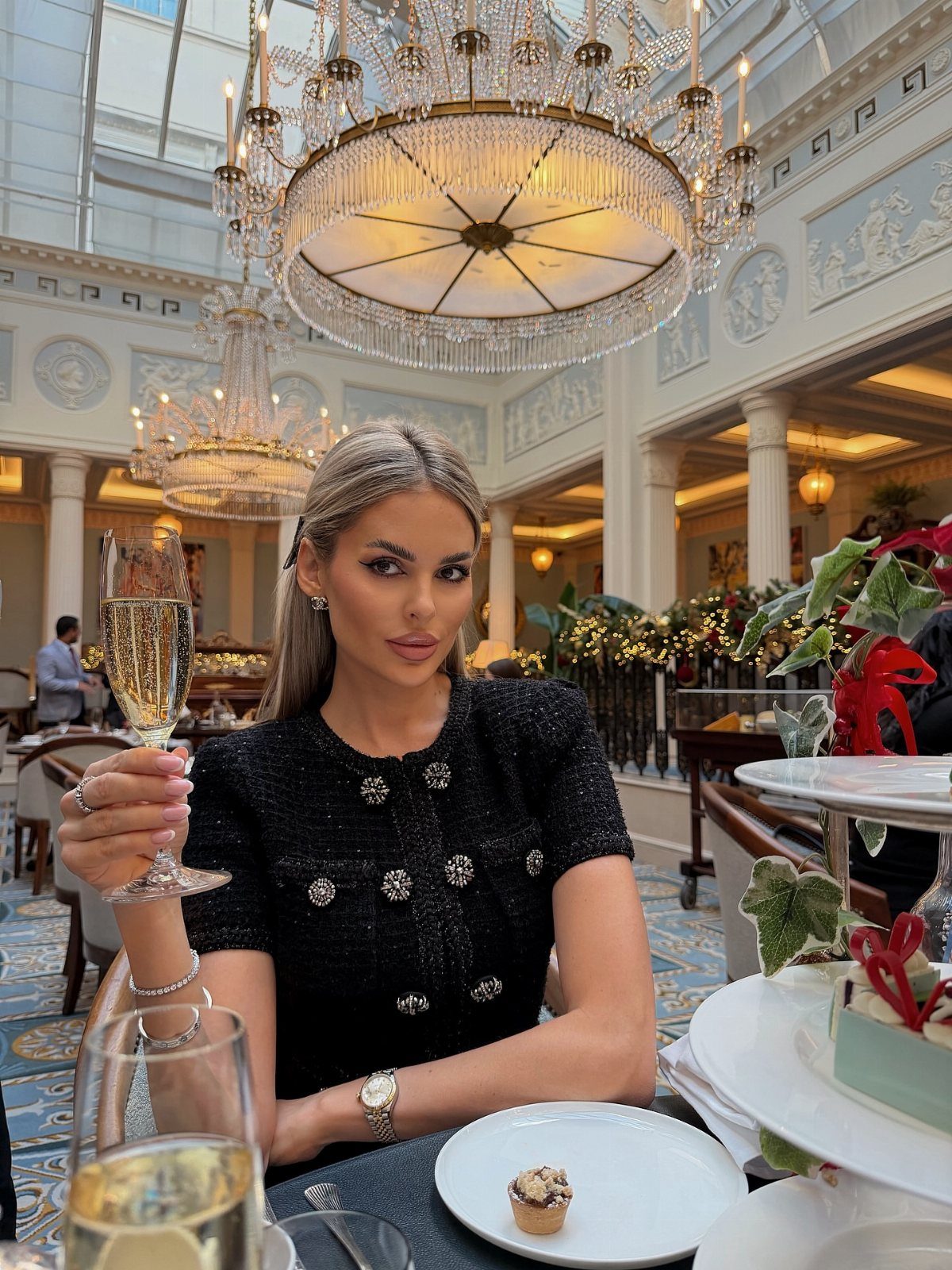 Woman in black dress holding champagne in a luxury hotel tea room