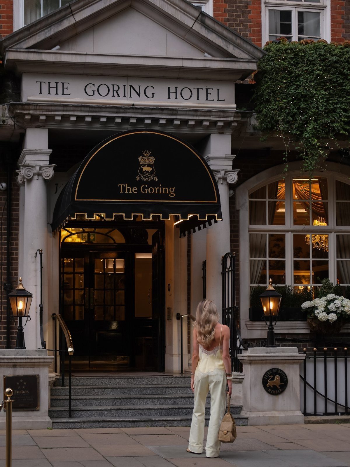 Woman in white jumpsuit standing outside the entrance of The Goring Hotel London