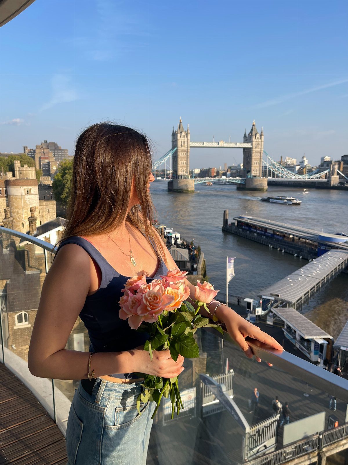 Woman holding pink roses on a balcony overlooking Tower Bridge in London