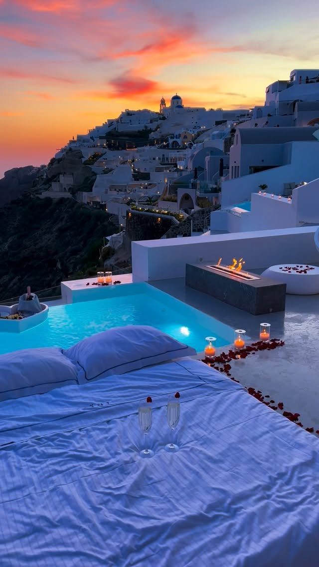 Luxury bedroom with plunge pool overlooking whitewashed Santorini buildings during a vibrant sunset.