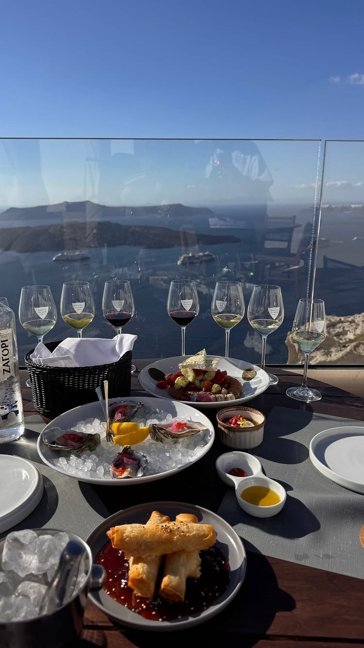 Wine glasses and appetizers on a table overlooking the Santorini caldera and sea.