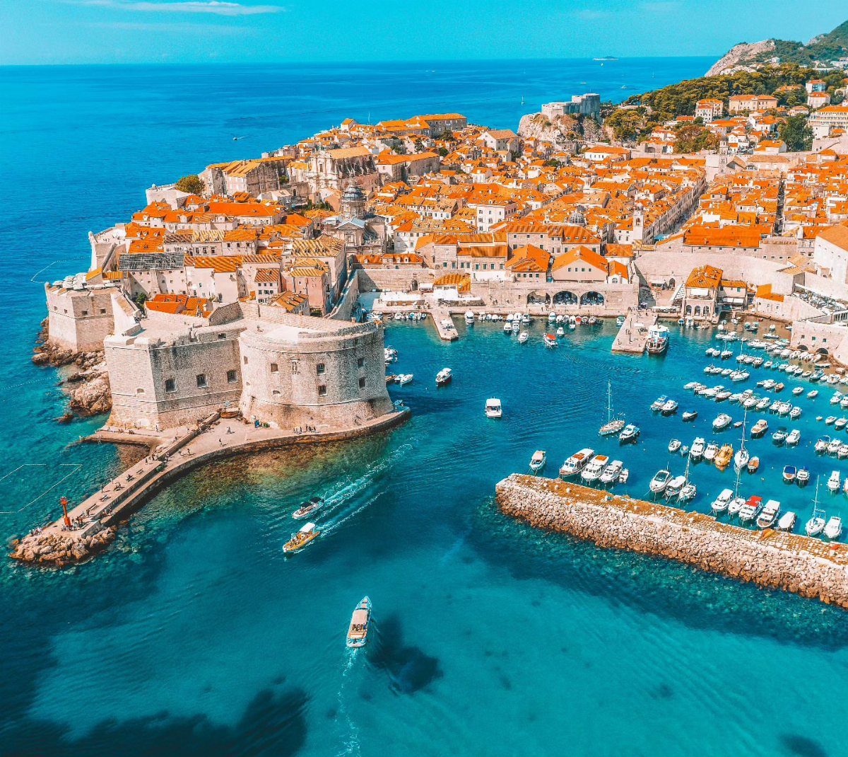 Ancient stone city walls surrounding a coastal town with orange roofs and turquoise water.