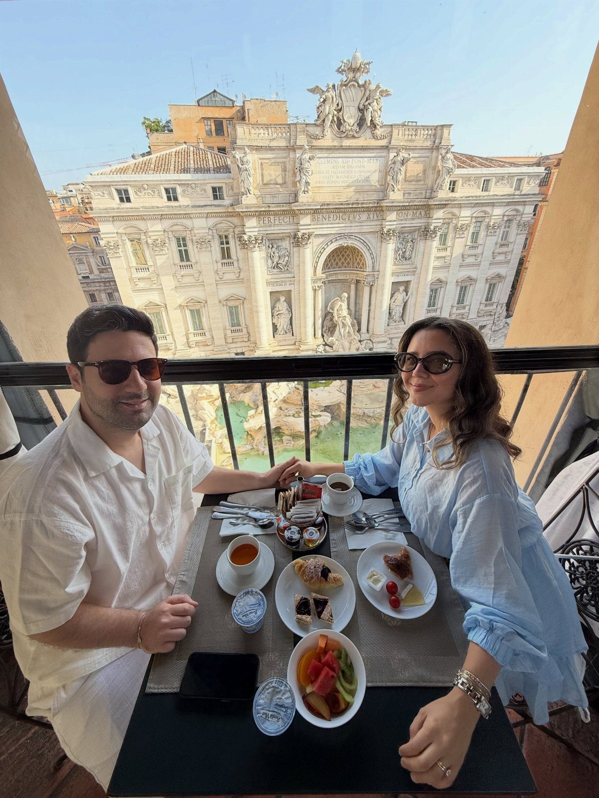 Couple holding hands at breakfast with the Trevi Fountain in Rome behind them.
