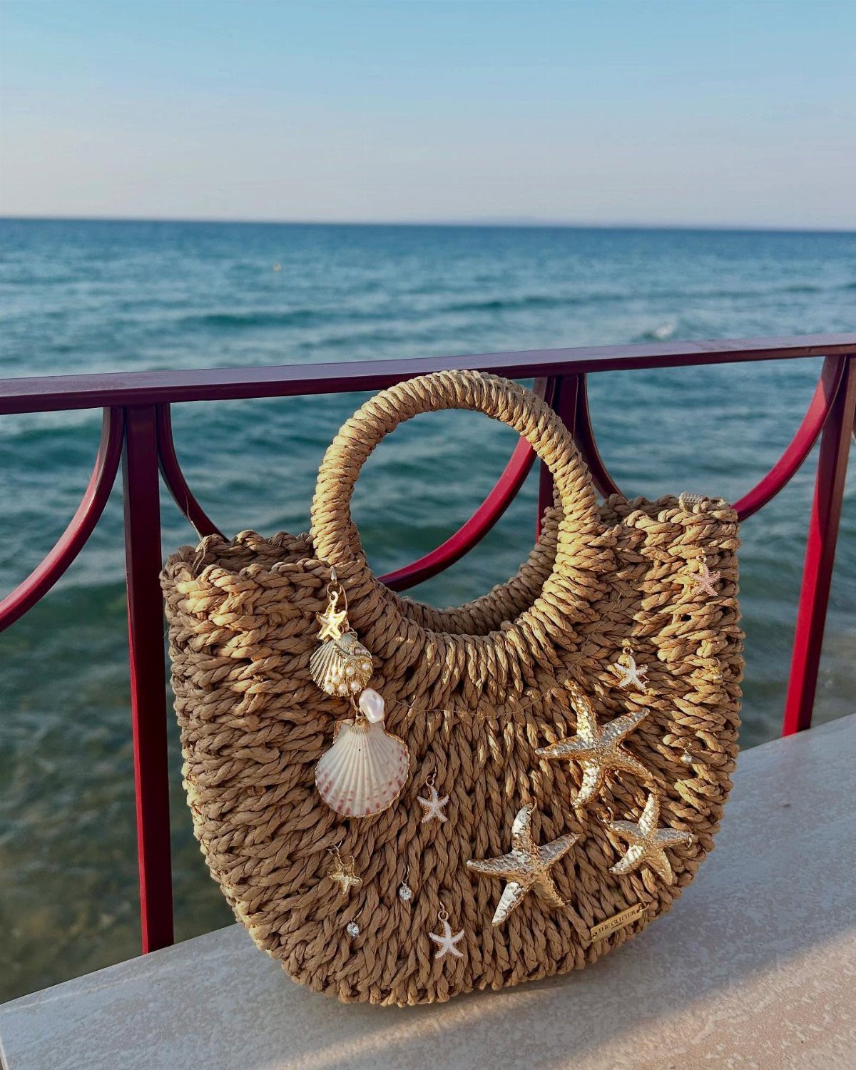 Woven straw beach bag with seashell and starfish decorations overlooking the blue ocean.
