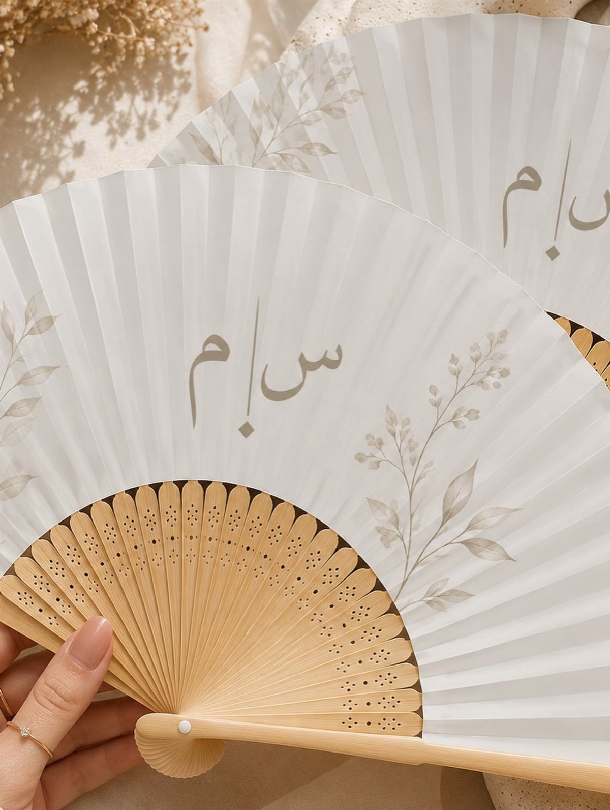 White folding hand fans with wooden ribs and Arabic calligraphy held by a hand.