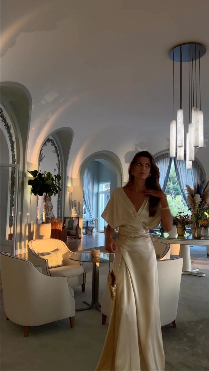 Woman in a long cream satin wrap dress standing in a modern white room
