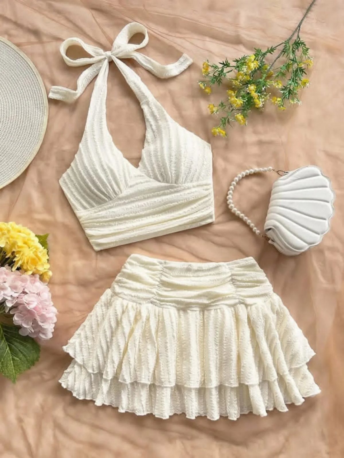 White halter crop top and ruffled skirt with straw hat and shell purse.