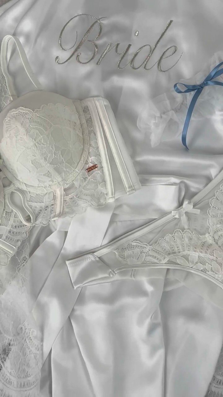 White lace lingerie and satin bride robe laid out on white fabric.