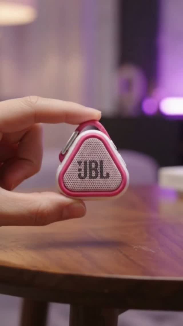 Small pink and white JBL portable speaker held by a hand over wooden table