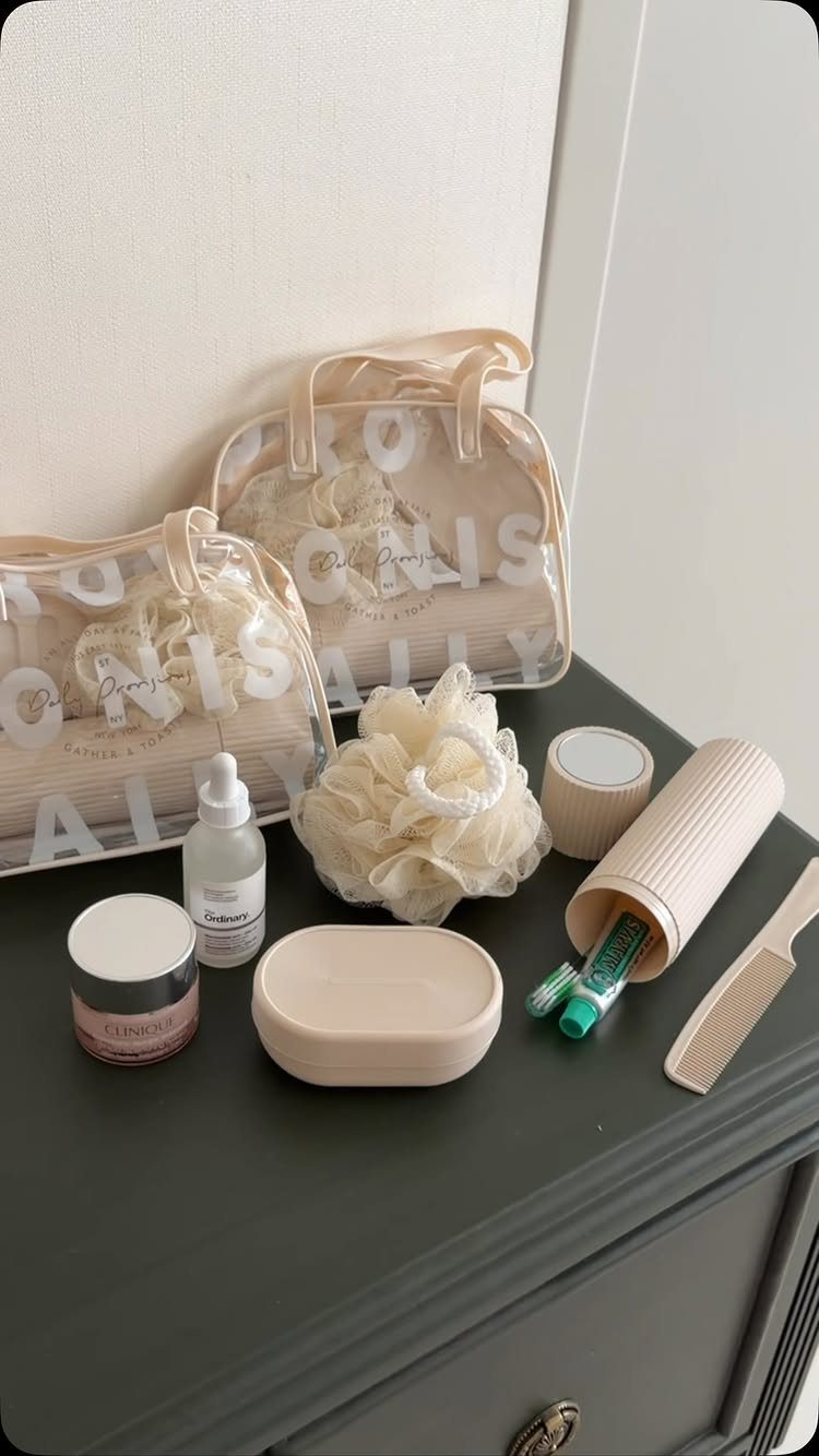 Beige skincare and beauty travel essentials arranged on a dark grey dresser surface.