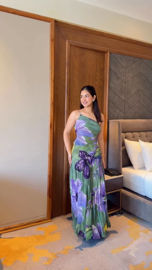 Woman wearing a long green and purple floral one-shoulder day dress in a hotel.