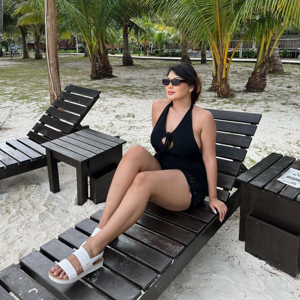Woman in black dress wearing white flat sandals on a beach lounge chair