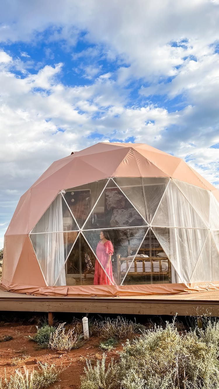 Woman in pink dress inside a geodesic dome tent in a red desert landscape