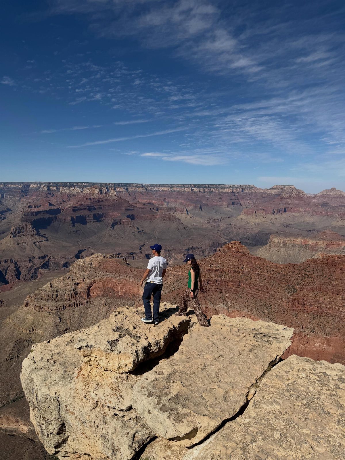 Two people standing on a rocky cliff overlooking the Grand Canyon's red vistas.