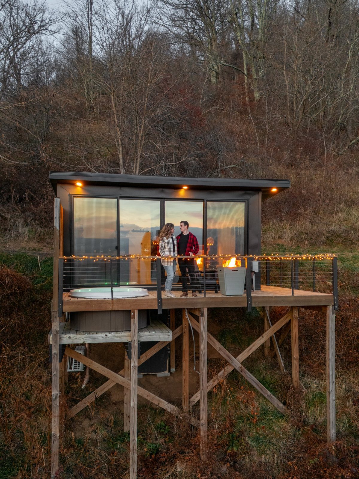 Couple standing on the deck of a modern tiny house cabin in the woods