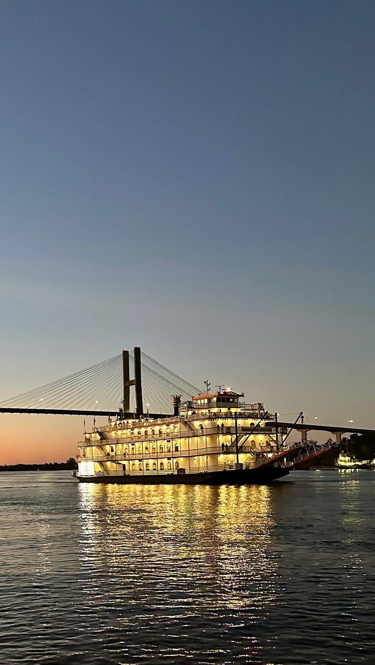 Illuminated paddle steamer boat on a river with a cable bridge at dusk
