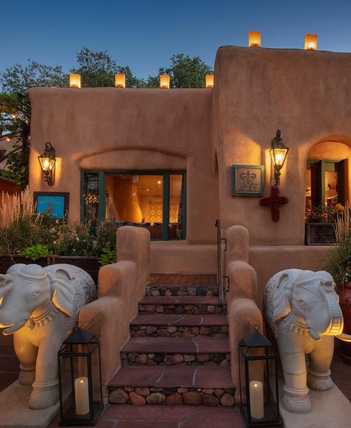 Adobe building with rounded walls, stone stairs, and white elephant statues at dusk.