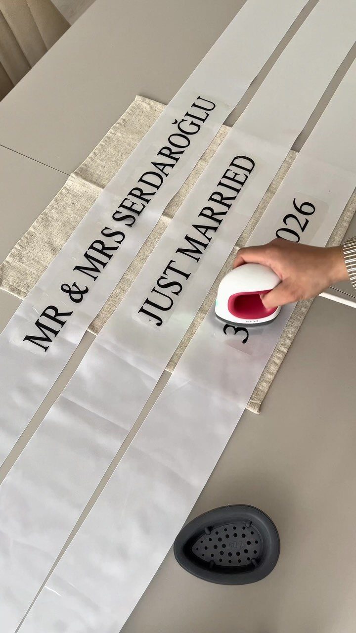 Hand ironing black Just Married lettering onto white fabric ribbons on a table