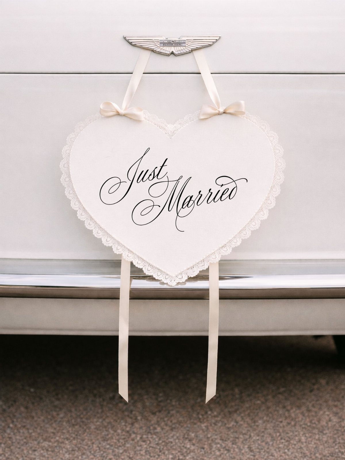 Heart-shaped white sign with black cursive Just Married lettering hanging on a car.