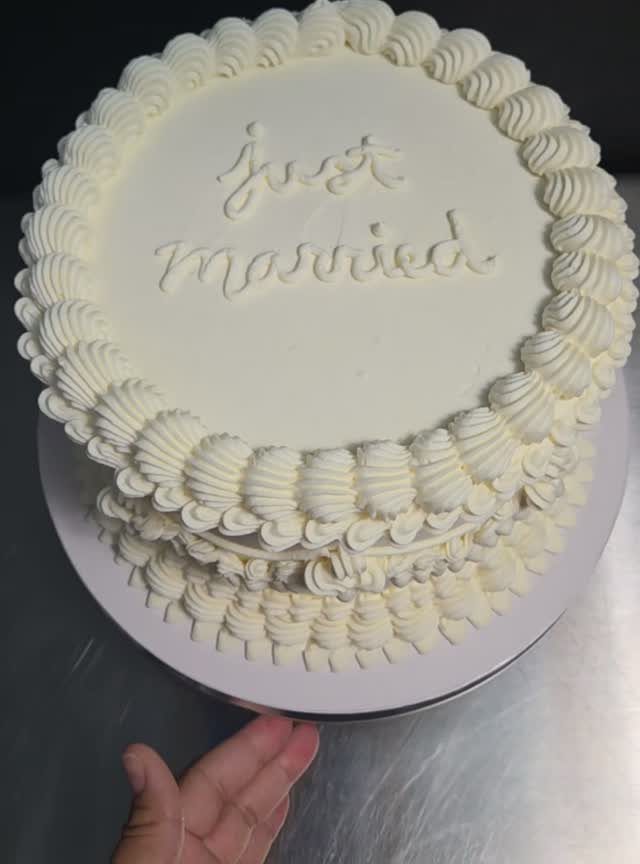 White frosted cake with just married written in cursive icing on top.