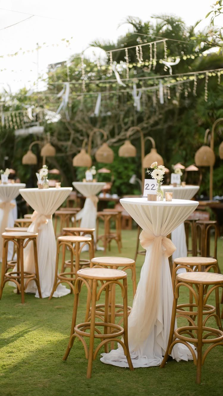 High-top cocktail tables with white linens and wooden stools on a lush lawn