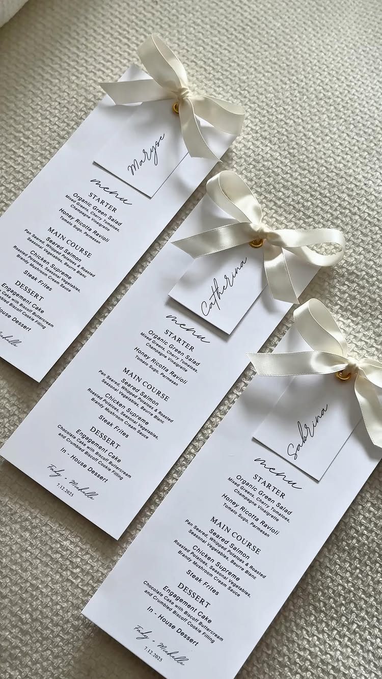 Three elegant white wedding menus with satin bows and personalized name cards.