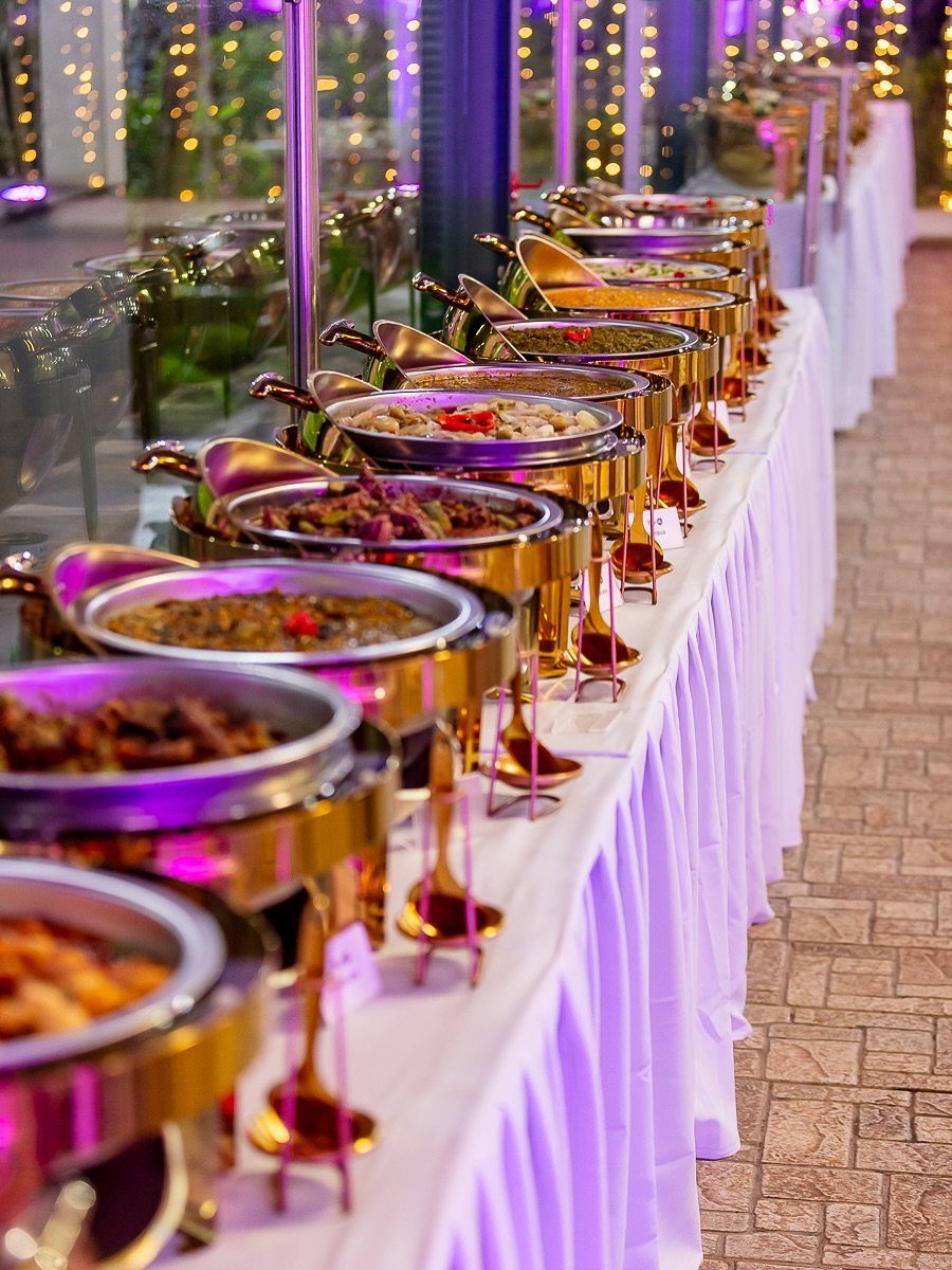 Gold chafing dishes with various foods on a white tablecloth at a wedding.
