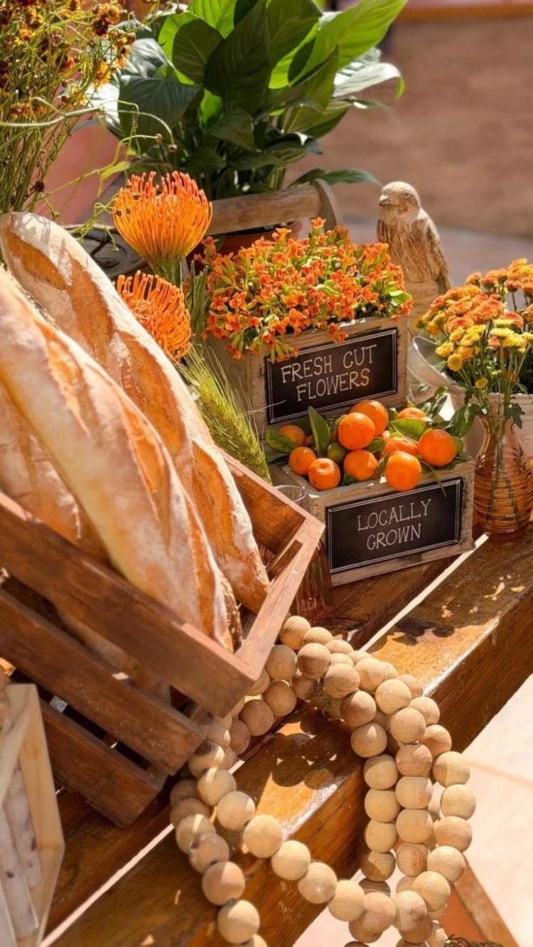 Rustic food display with baguettes, oranges, and orange flowers on a wooden table.
