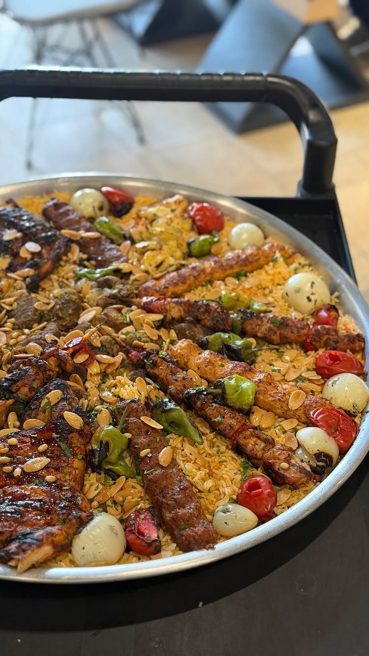 Large metal platter of yellow rice topped with grilled meats and roasted vegetables.