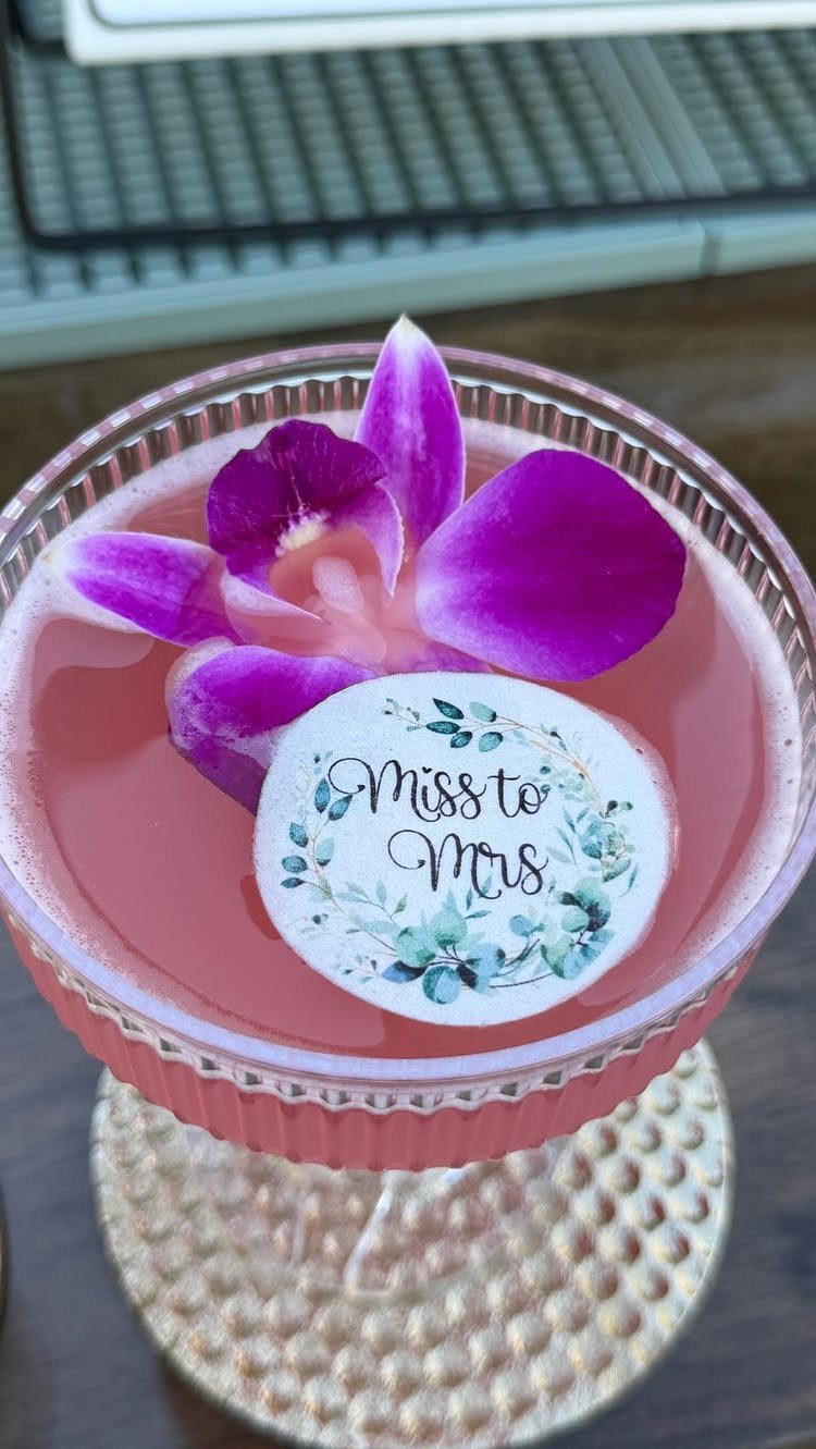 Pink cocktail garnished with a purple orchid and a Miss to Mrs wafer.
