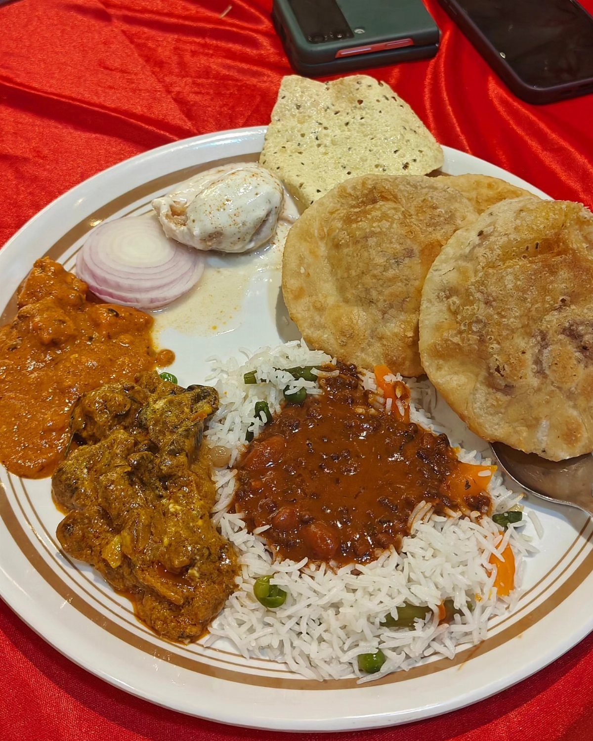Indian meal with rice, curry, puris, and raita on a red tablecloth