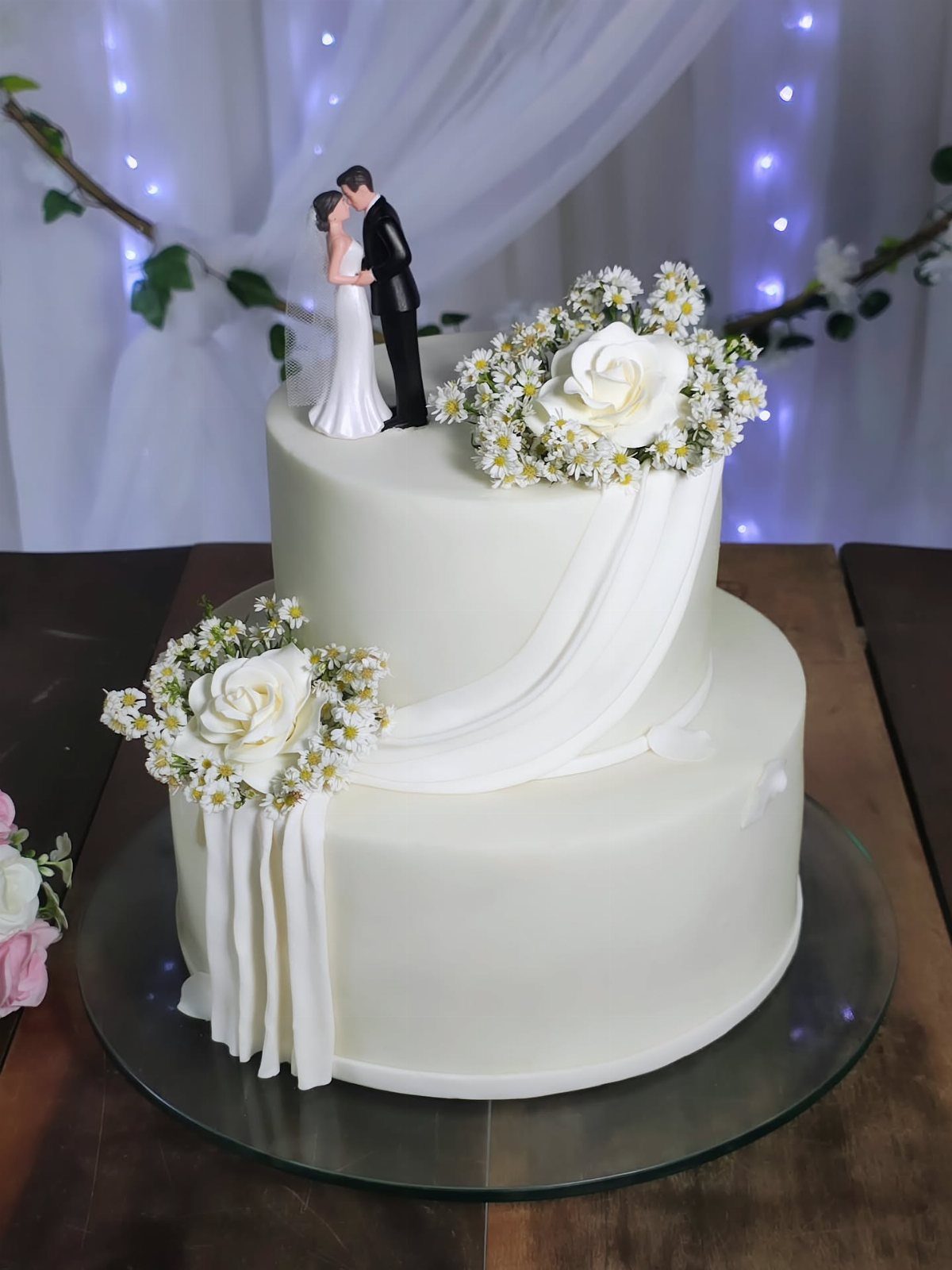 Two-tier white wedding cake with floral decorations and a bride and groom topper.